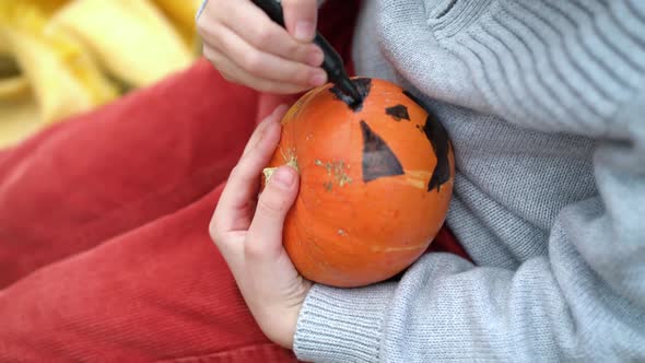 Close Up Boy Hands Paint Orange Pumpkin with Black Paint in Autumn Forest