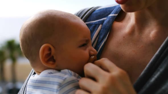 Young mother consoling crying baby in sling at home