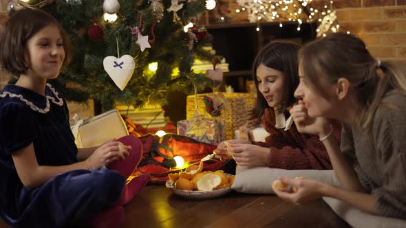 Mom and Two Daughters Having Good Times Together Eating Mandarines Under Christmas Tree at Home