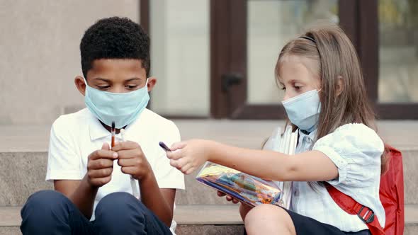 Two Kids in Uniform and Protective Masks Writting in Notebooks Sitting on Stairs Near School