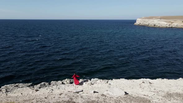Brunette Woman in a Red Long Dress Walk on the Edge of a Cliff By the Sea