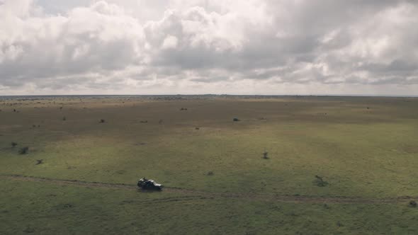 Man sitting on top of 4 wheel drive while on wildlife safari adventure in Kenya. Aerial drone view