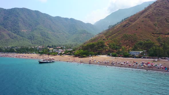 aerial drone view of Adrasan beach full of people as a boat is anchored on the beach waiting for tou