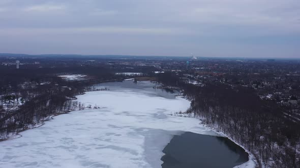 An aerial view from a drone, over a frozen lake during sunrise on a cloudy morning. The camera boom