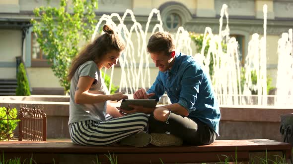 Young Loving Couple Sitting By the Beautiful Fountain