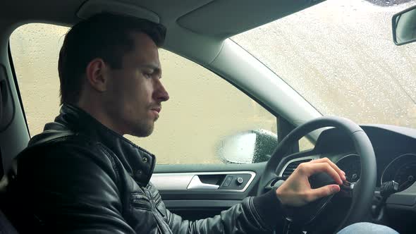 Young Handsome Sad Man Sits in Car on Place for Driver and Observes Landscape