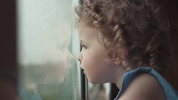A cute three-year-old girl looks out for something in the window