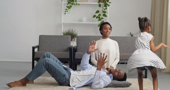 Afro American Family Having Fun at Home on Weekend Little Girl Jumping Around Room Flapping Her