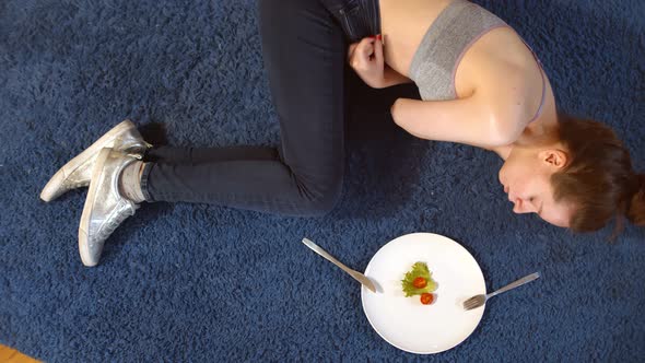 Sad Woman Having Anorexia Nervosa Having Small Green Vegetable and Tomato on Plate Lying on Floor