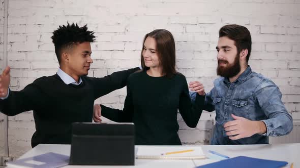 Multiethnic Diverse Business Team Embracing Each Other While Sitting at the Table in Modern Office