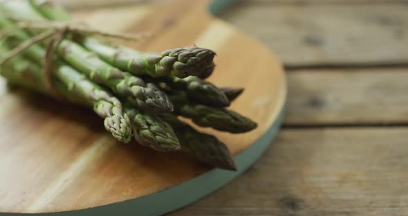 Video of close up of fresh asparagus bundles on wooden board background