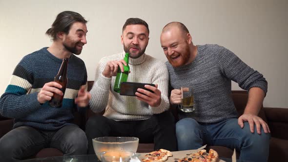 Three Cheerful Men Rejoice Watching Videos on Smartphone Sitting at Home During