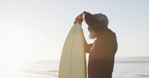 Happy senior african american man holding surfboard on sunny beach