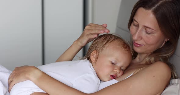 Young Beautiful Mother Hugs Baby Daughter Who Sleeps on Her at Home