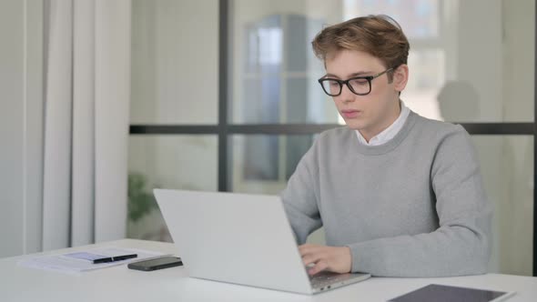 Young Man Looking at Camera While Using Laptop in Modern Office
