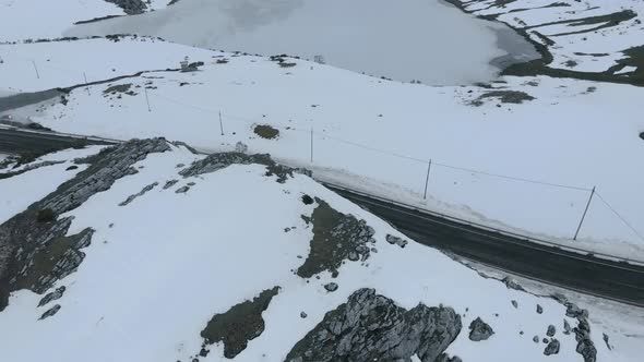 Drone aerial view above Isoba lake, frozen snowy road in valley of stony mountains, pale and white w