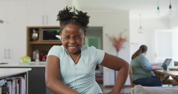 Happy african american girl wearing earphones and dancing in living room