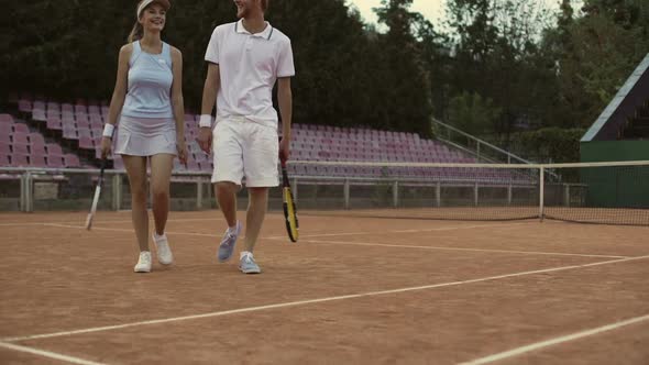 Man and woman in white sportswear walking on court, preparing to play tennis