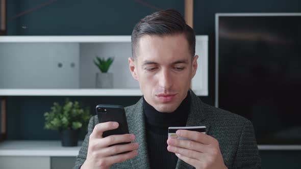 Happy Businessman Shopping Online on His Smartphone and Paying with Credit Card at Modern Office