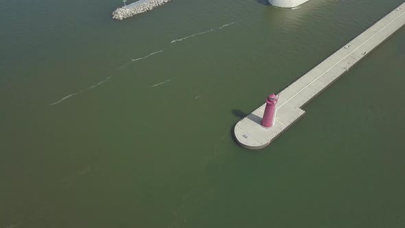 Aerial view of freighter moving out of canal in Michigan, USA. Beacon on pier visible. Drone moves b