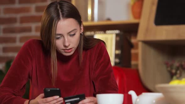 Joyful Young Woman Texting Message To Friend As Resting in Cozy Stylish Kitchen, Using Smartphone