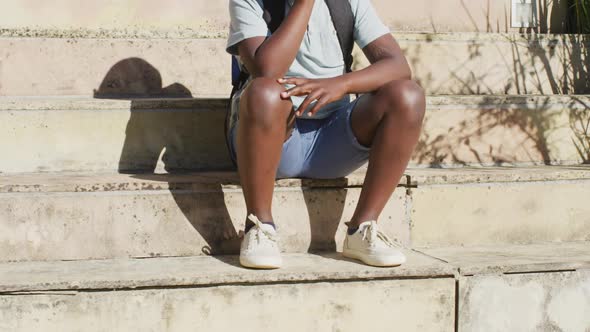 Sad african american boy wearing face mask sitting on stairs outdoors on a sunny day