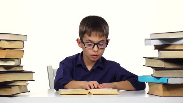Little Boy Sits at a Table and Reads the Book Slowly. White Background