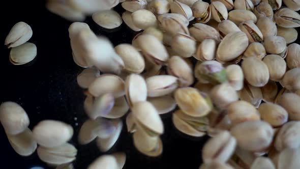 Pistachio nuts fall on a black mirror surface