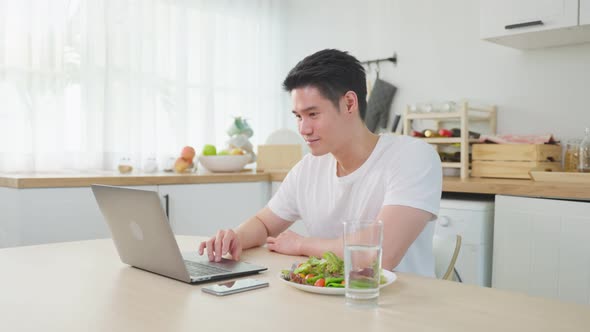 Asian business man eating healthy green salad while working from home.