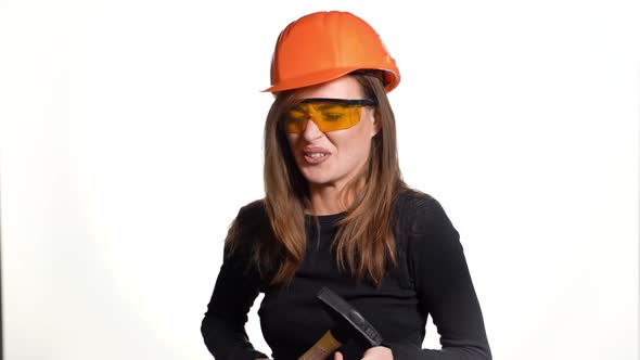 Beautiful Woman in Orange Eyeglasses and Helmet is Holding a Hammer in Her Hands 