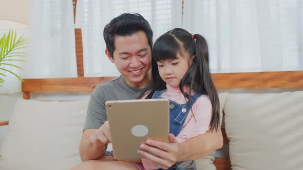 Asian loving father with little girl using tablet learning from home and playing internet online.