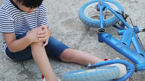 Sad little girl sitting on the ground after falling off her bike at summer park.