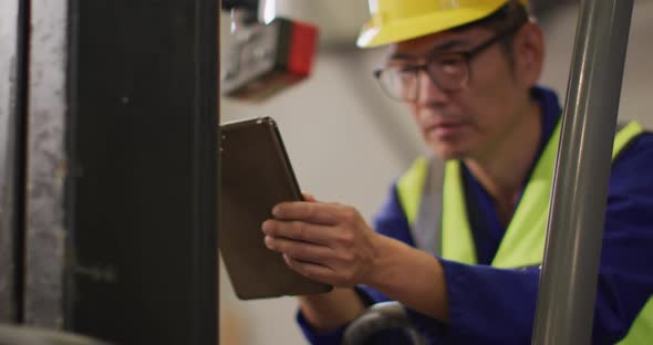 Asian male worker wearing safety suit with helmet using tablet in warehouse