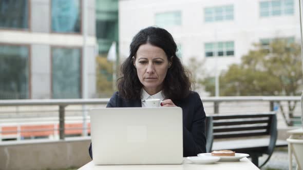 Businesswoman Using Laptop and Drinking Coffee in Cafe