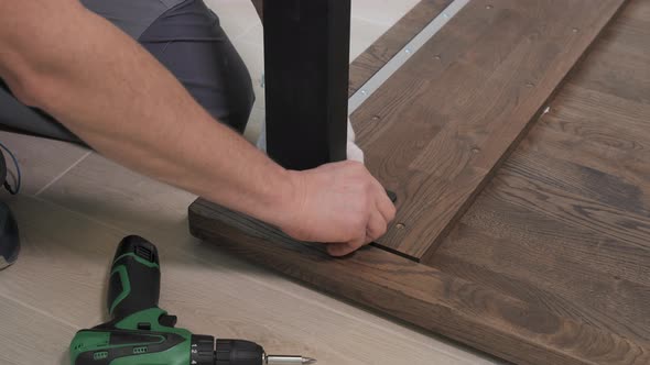 Builder in Overalls Screwing Table Legs Using a Screwdriver