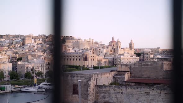 Camera moves behind metal fence showing part of Malta's famous Three Cities