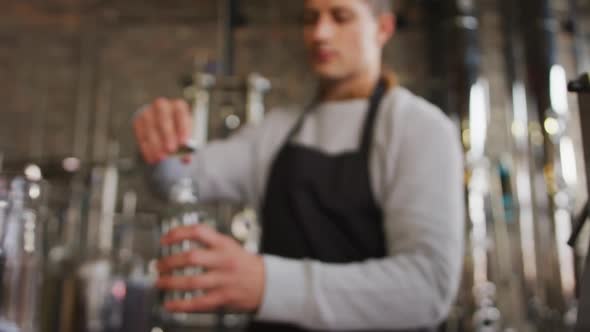 Caucasian man working at gin distillery, wearing apron, fastening lid on bottle of gin