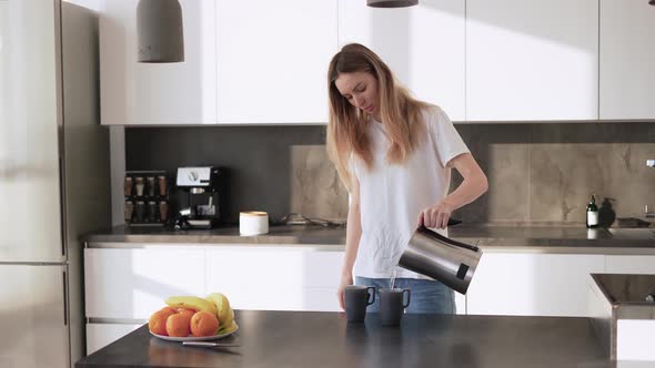 A Young Woman Pours Tea Into a Cups From a Kettle