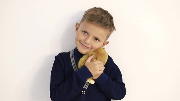 Beautiful Little Boy with a Soft Toy on a White Background Tenderly Hugs the Toy