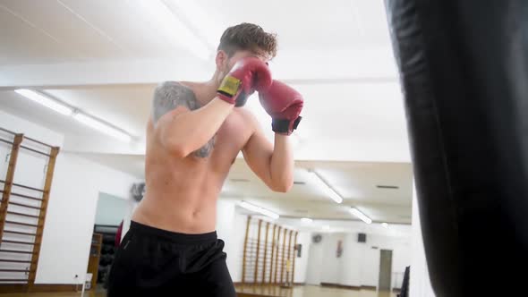 Young guy trains in a gym and fists his boxing bag fist