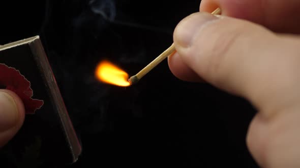 The match moves on the side of the matchbox and light the fire. Closeup. Shallow depth of field. Slo