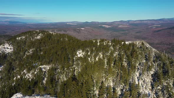 Aerial slide to the left past a snow dusted mountain peak in Maine