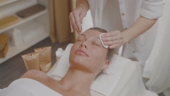 Cosmetologist Applies Tonic with Cotton Pads to Skin of Faceneckdecollete