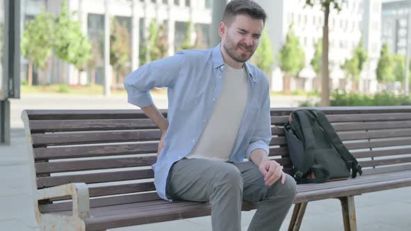 Young Man Having Back Pain While Sitting on Bench