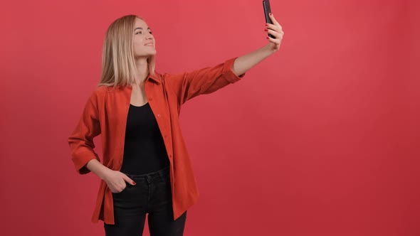 Funny Young Blonde Haired Woman Taking Selfie on Red Background.