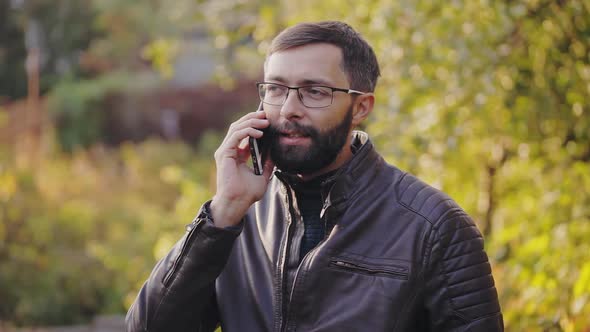 Bearded Man Uses a Mobile Phone in Sunny Autumn Park