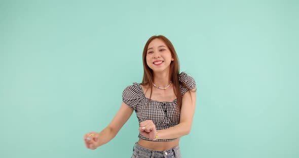 Happy carefree Asian woman dancing and looking at the camera over green background