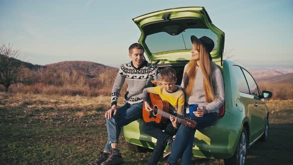 Family Plays Guitar and Sings Songs While Sitting on the Hatchback of the Car