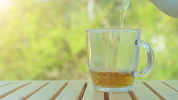 Tea pouring into cup from teapot on green nature background