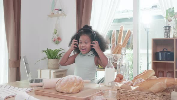 Little African girl student wearing headphones online to study on a laptop, in the kitchen at home